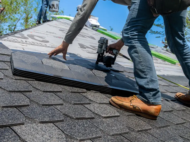 A roofer running a nail gun along a course of asphalt shingles on a residential roof