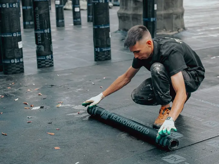 A worker rolling waterproof membrane across a low-slope commercial roof