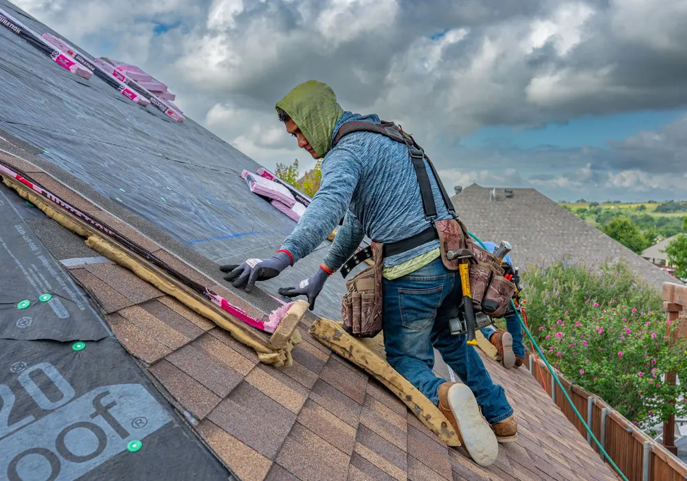 A roofer in a harness laying a course of architectural shingles over underlayment on a steep residential roof