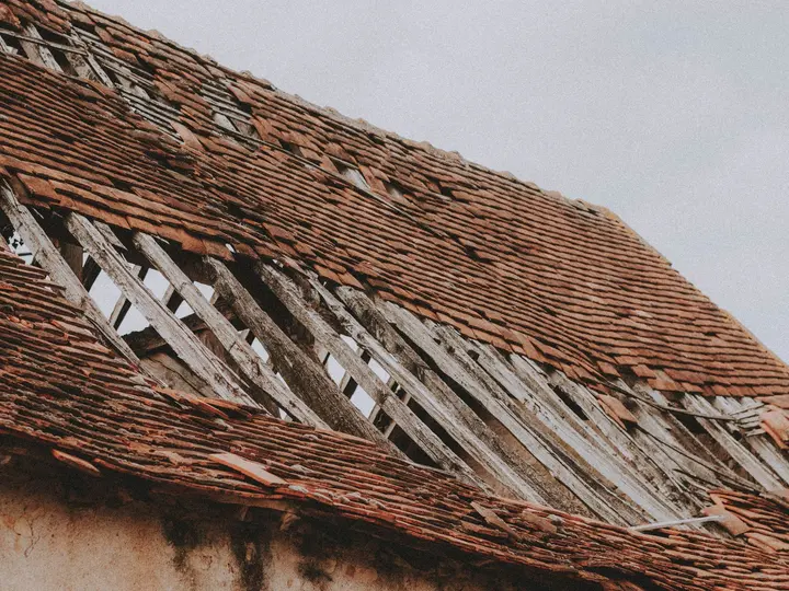 A damaged roof with shingles torn away and bare decking showing underneath